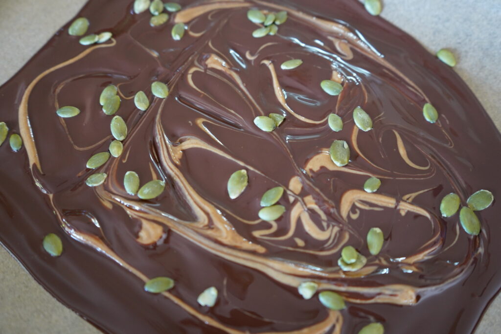 pumpkin seeds added to melted chocolate on parchment paper