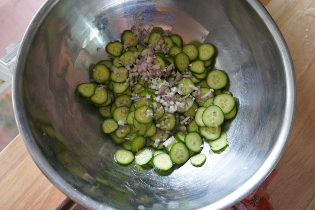 a bowl full of sliced cucumbers with chopped shallots on top