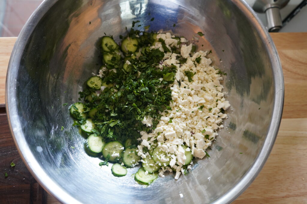chopped cilantro added to a bowl of cucumbers and feta
