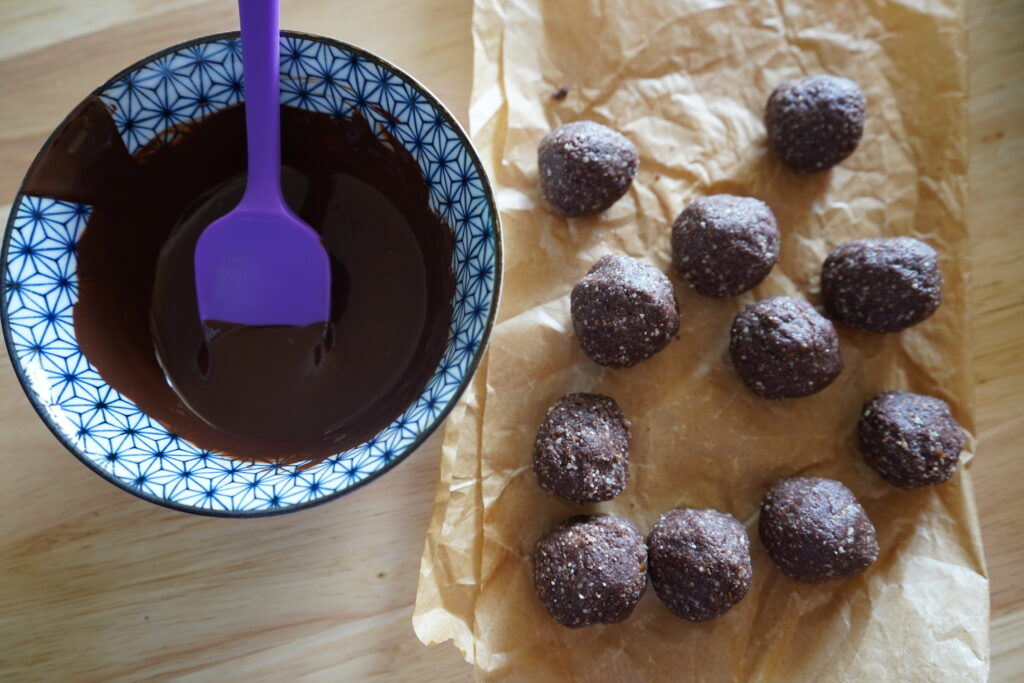 melted choclate in a bowl next to date balls