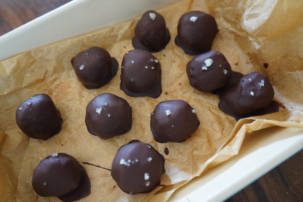 chocolate covered date balls on parchment paper with flaky salt on top