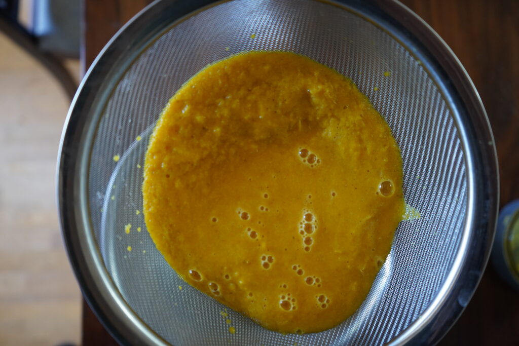 a mesh strainer straining orange juice into a bowl