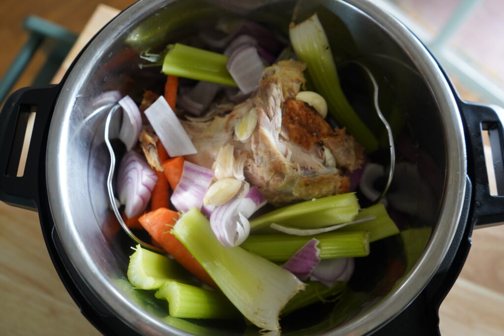chicken bones being covered by vegetables in an instant pot