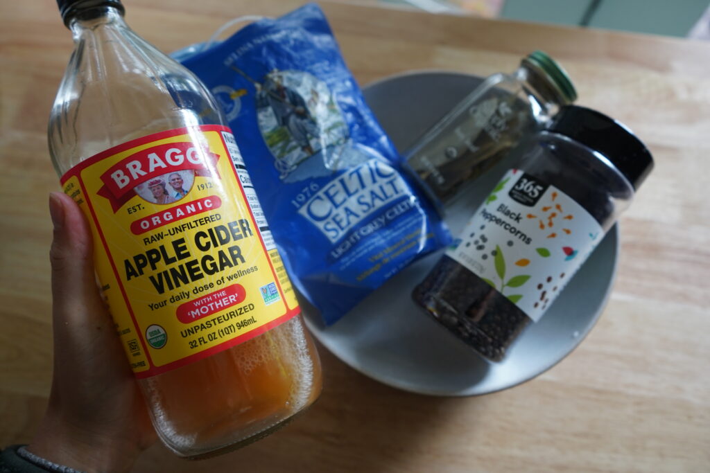 a hand holding apple cidar vinegar next to ingredietns in a bowl
