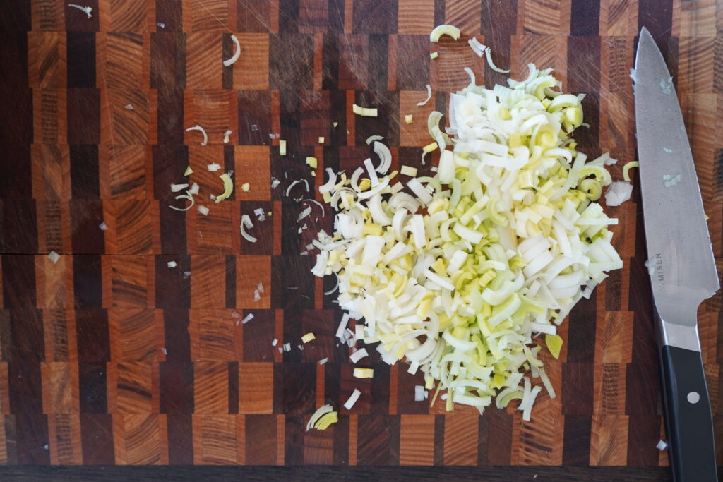 chopped leeks on a cutting board next to a knife