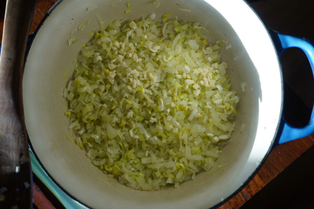 minced garlic on top of chopped leeks and onions in a pot
