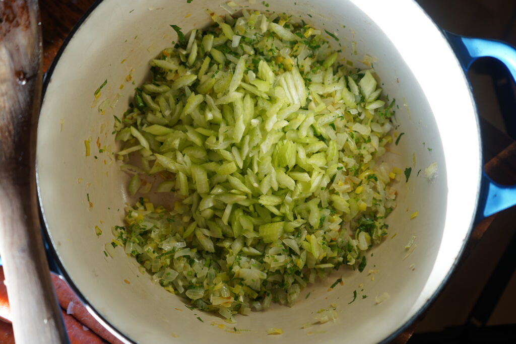 celery added to a pot with cooked onions and leeks