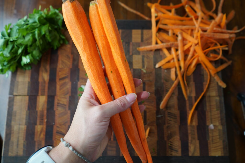 peeled carrots being held in a hand over a cutting board