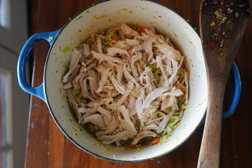shredded chicken added to a blue pot of cooked vegetables