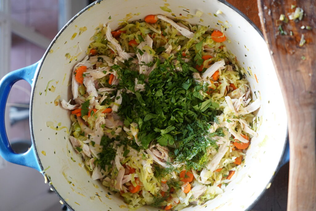 chopped dill and parsley being added to a blue pot of vegetables