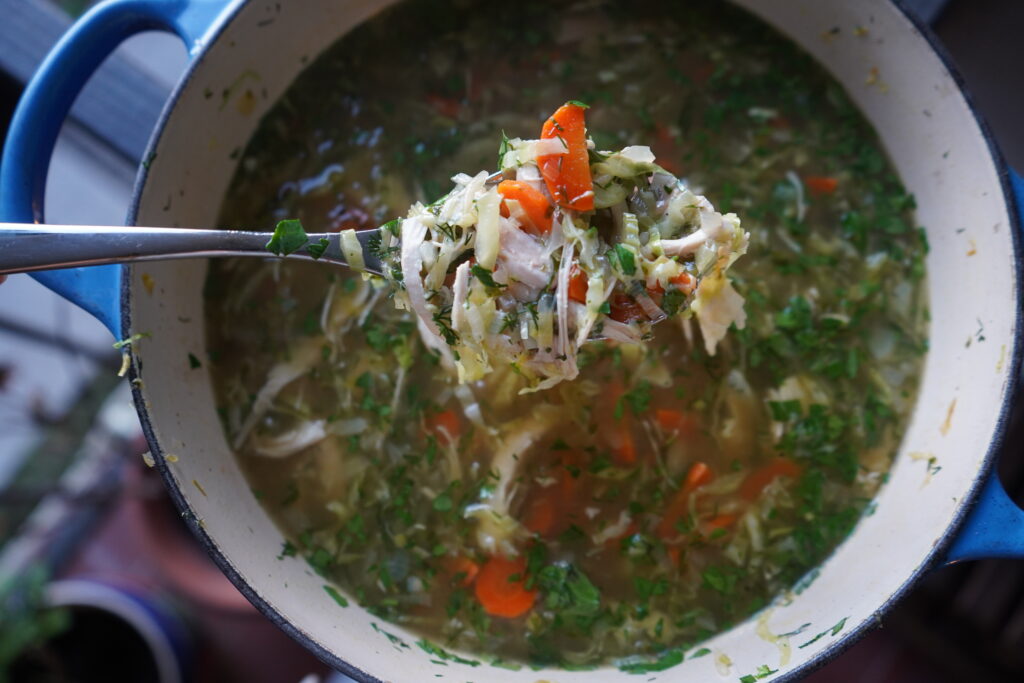 chicken and cabbage soup being spooned out of a blue dutch oven