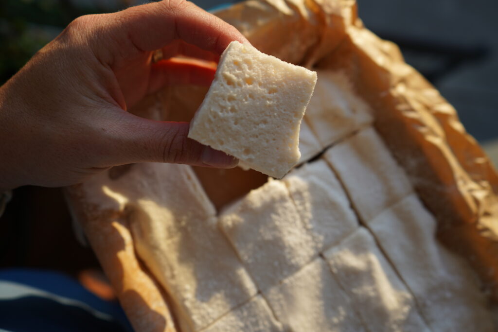 a hand holding a homemade marshmallow over a tray of marshmallows