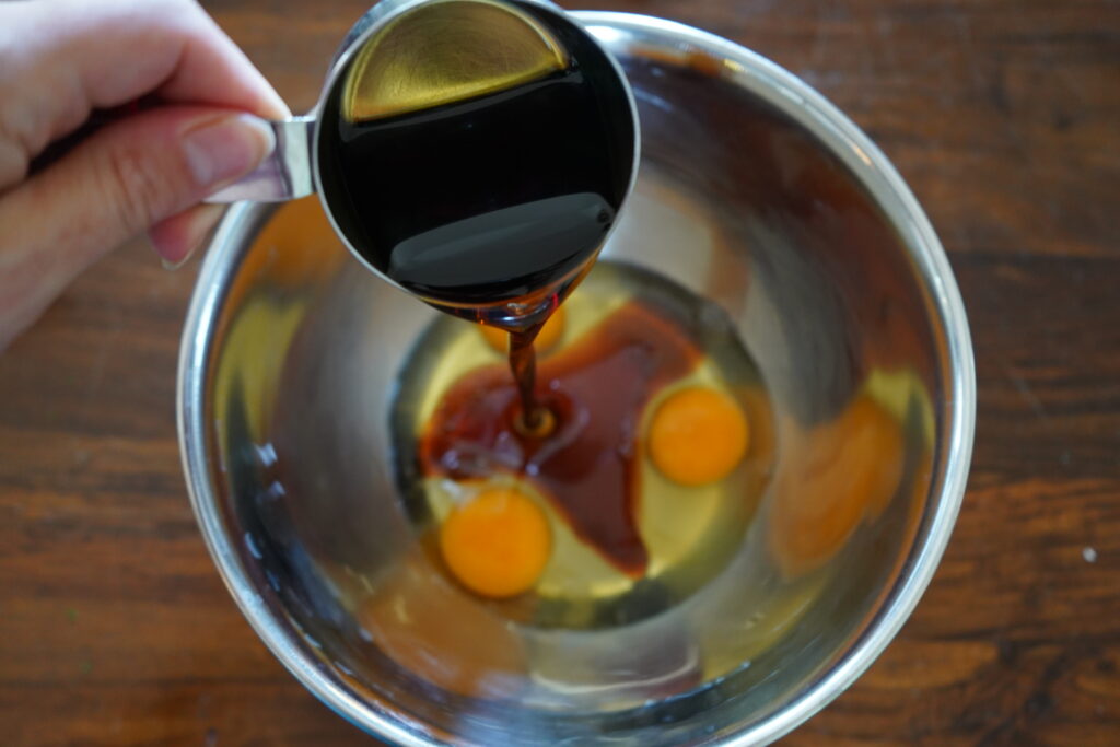 maple syrup being poured into a mixing bowl of eggs