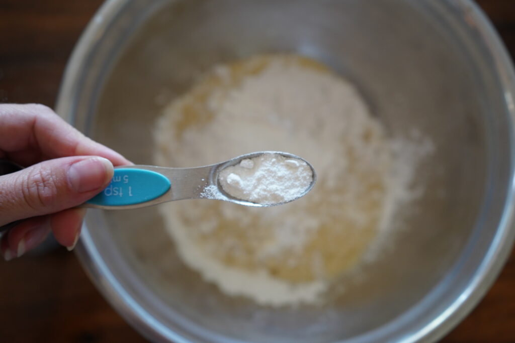 baking powder being added to a bowl of dry ingredients for muffins