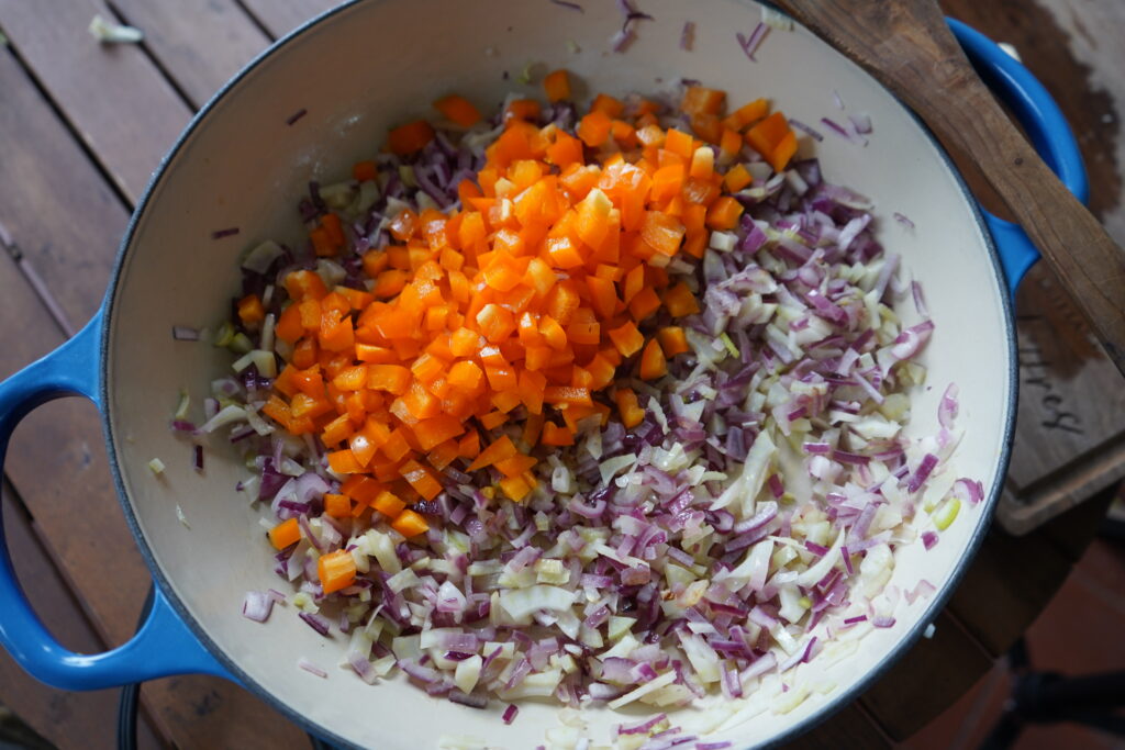 chopped orange bell pepper added to a skillet of vegeatbles