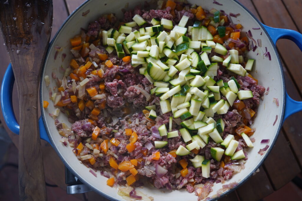 a ground beef and vegetable skillet with zucchini added to the pan