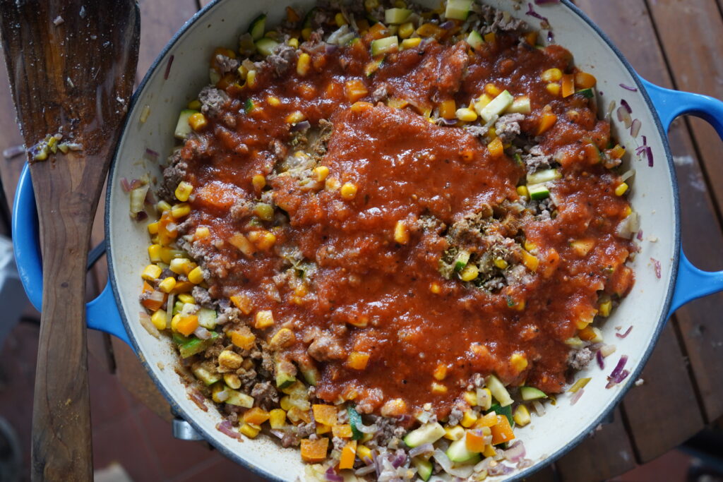 enchilada sauce on top of a skillet of meat and vegetables