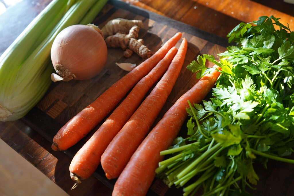 celery, onion, carrot and parsley on a cutting board being prepared for chicken noodle soup