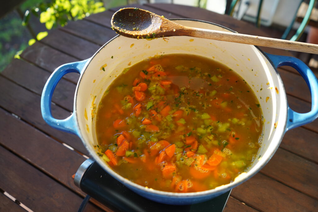 bone broth being added to a pot of sauteed vegetables