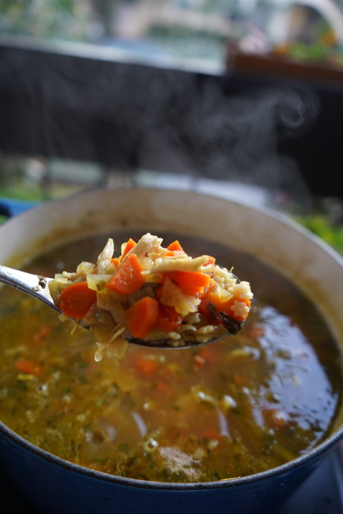chicken noodle soup being spooned out of a dutch oven